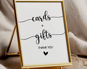 May include: A gold-framed sign with the text "cards + gifts" in black cursive lettering. The sign also includes the text "Thank You" and a small black heart.