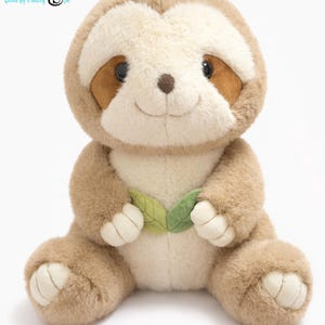 May include: A plush sloth toy in shades of brown and cream, with a smiling face and two green leaf accents. The toy is sitting with its legs extended and has the text "MATIAN" in the upper left corner.