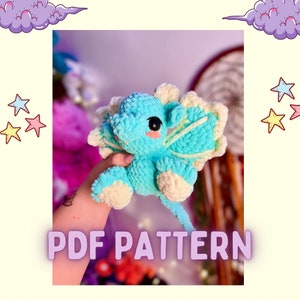 May include: A crochet pattern for a light blue dragon with white wings and a tail. The pattern is available as a PDF download. The text "PDF PATTERN" is printed on the image.