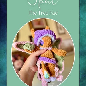 Puede incluir: Un juguete de peluche tejido a crochet con un sombrero y alas moradas. El juguete es marrón con una cara marrón claro y tiene una hoja verde en su mano. El juguete está etiquetado como "Opal The Tree Fae".