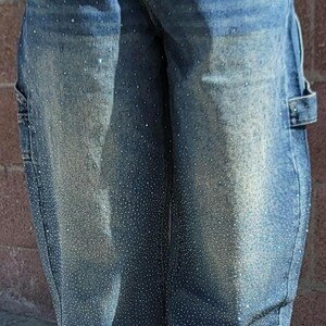 May include: Blue denim jeans with a light wash and rhinestones. The jeans have a relaxed fit and a wide leg.