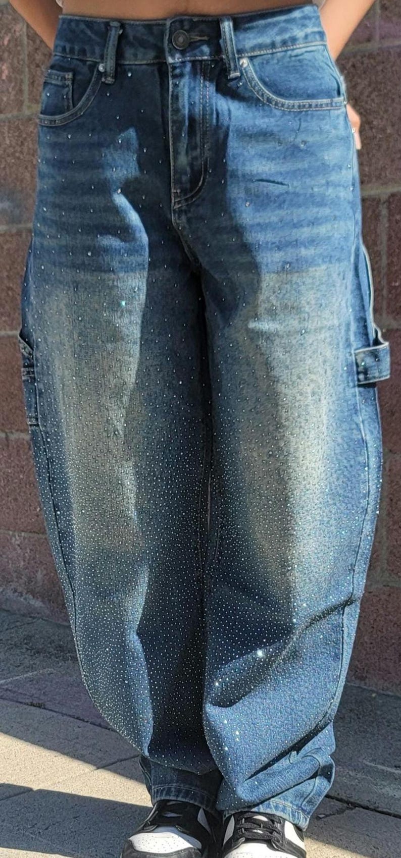 May include: Blue denim jeans with a light wash and rhinestones. The jeans have a relaxed fit and a wide leg.