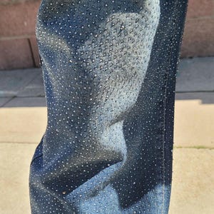 May include: Close-up of blue denim jeans with a pattern of small, silver rhinestones.
