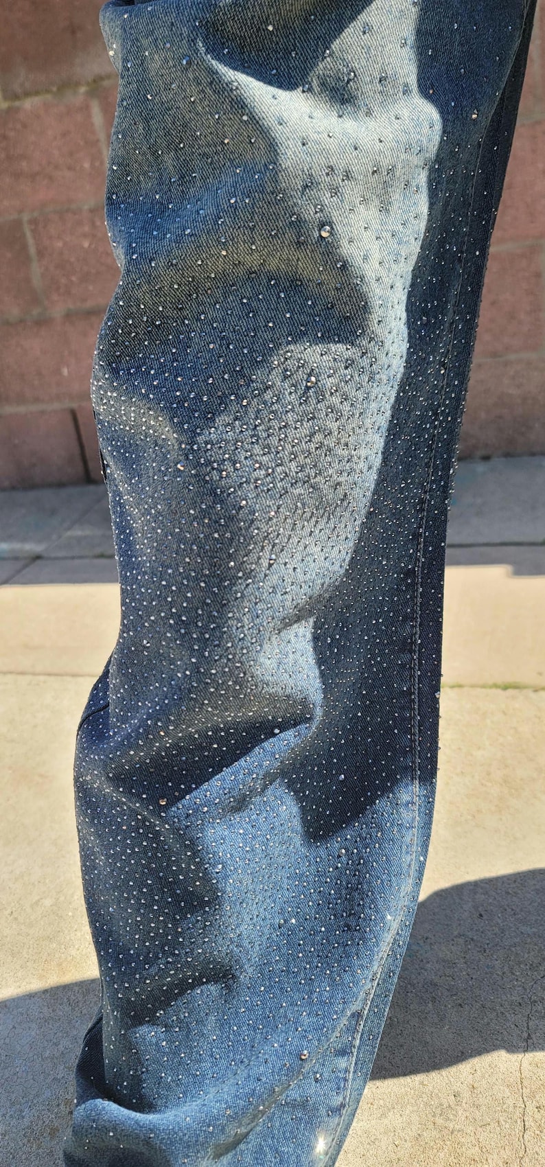 May include: Close-up of blue denim jeans with a pattern of small, silver rhinestones.