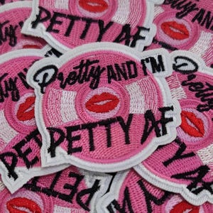 May include: Pink embroidered patch with the words "Pretty AND I'M Petty AF" in black lettering. The patch features a pink and white design with a red lip graphic. The patches are scattered across the image.