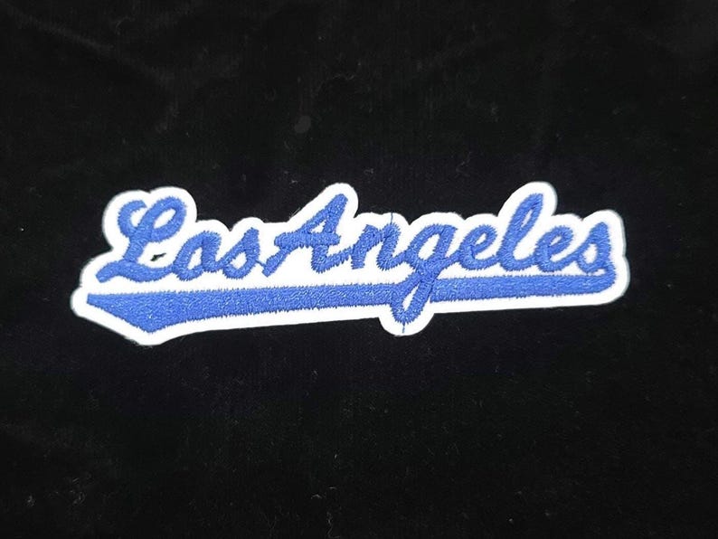Pu&ograve; includere: Toppa ricamata con la scritta "Los Angeles" in blu, in corsivo e bordata di bianco. Il testo &egrave; posto su uno sfondo nero. Ideale per personalizzare abbigliamento o accessori.
