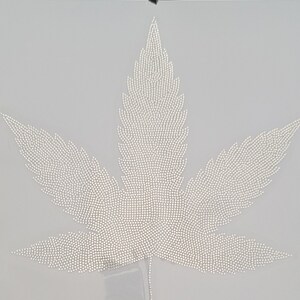 May include: A white marijuana leaf design made of small white rhinestones on a white background.
