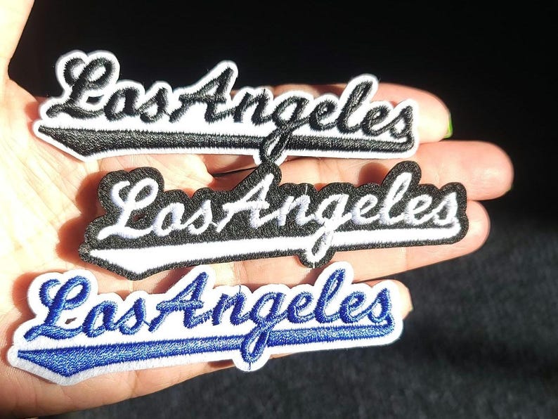 Pu&ograve; includere: Tre toppe ricamate con la scritta "Los Angeles" in un carattere corsivo. Le toppe sono in bianco e nero e in blu e bianco. Le toppe sono probabilmente per abbigliamento o accessori.