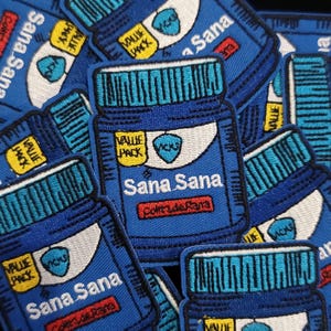 May include: Embroidered blue patches featuring a stylized jar design with the text "Sana Sana" and "Cortade Rana". Each patch includes a "Value Pack" label and a "Vicks" logo. The patches are a vibrant blue with white, yellow, and red accents.