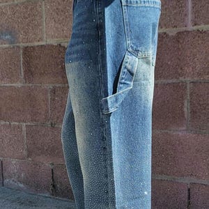 May include: A pair of blue denim carpenter jeans with rhinestones. The jeans have a relaxed fit and a wide leg.
