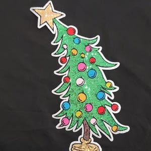 May include: A whimsical Christmas tree design with a gold glitter star on top and colorful ornaments. The tree is green with a silver glitter outline, set against a black background. The base of the tree is gold.