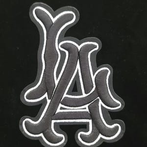 May include: Embroidered patch in black and white, displaying the letters "LA" in a decorative font. The black letters have a white border, set against a black backdrop. Ideal for customising clothing or accessories.