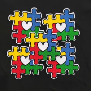 May include: A colorful patch featuring a puzzle design with yellow, red, blue, and green pieces. Each piece has a white heart in the center. The patch is on a black background.