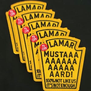May include: A stack of yellow embroidered patches in the shape of a mustard bottle. Each patch has black text that reads "LAMAR" and "MUSTAAA AAAAA AAAAA AARD!" with "100% NOT LIKE US IT'S NOT ENOUGH" at the bottom. A red "TV OFF" button is also present.