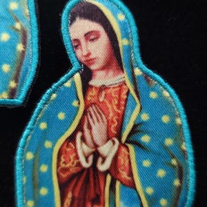 May include: Embroidered patch featuring a depiction of the Virgin Mary, wearing a blue and yellow robe with white polka dots, and holding her hands in prayer.