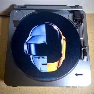 May include: A black vinyl record with a graphic of a robot's head, half silver and half gold, on a turntable.