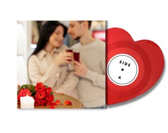 May include: A heart-shaped red vinyl record with a white center label featuring the text SIDE A in black. The record is displayed next to a square photograph showing a couple toasting with red drinks near a bouquet of red roses and a white candle.