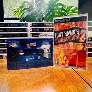 May include: A collection of PlayStation 2 video games and a custom cassette tape. The game cases are clear with black text. The cassette tape has a blue and black design with the text "TONY HAWK'S UNDERGROUND 2" and "Side A".