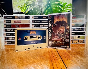 May include: A collection of vintage PlayStation video game cases and a cassette tape. The cassette tape features the game "DOOM" with a blue and beige design. The game case to the right is also "DOOM". Other game titles are visible.