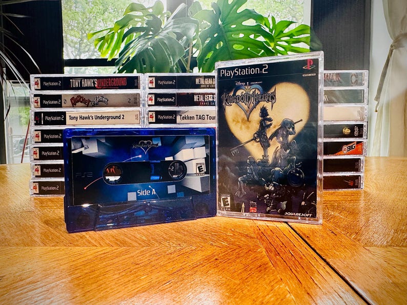 Peut inclure: Plusieurs jeux vid&eacute;o PlayStation 2, dont "Kingdom Hearts" et "Tony Hawk's Underground 2", sont pr&eacute;sent&eacute;s sur une surface en bois. Une cassette bleue avec le texte "Side A" est au premier plan. Les jeux sont dans des bo&icirc;tiers transparents.