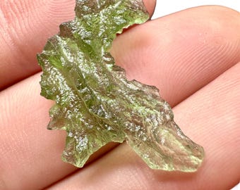 May include: A green, translucent, irregularly shaped piece of Moldavite, a type of tektite, a natural glass formed from the impact of a meteorite.