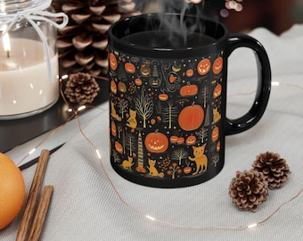 Puede incluir: Taza de cerámica negra con un diseño temático de Halloween. El diseño presenta calabazas naranjas, gatos, árboles y otros elementos festivos sobre un fondo negro. La taza tiene un asa negra y está llena de un líquido oscuro humeante.
