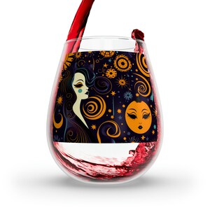 Puede incluir: Una copa de vino sin tallo con un diseño colorido que presenta la cara de una mujer, una luna y patrones en espiral en tonos naranja, amarillo, azul y negro.