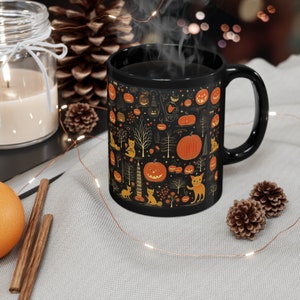 Puede incluir: Taza de café de cerámica negra con un diseño de temática de Halloween. La taza presenta un patrón repetitivo de calabazas naranjas, gatos negros y árboles dorados sobre un fondo negro.