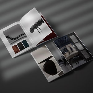 May include: Two open magazines displaying interior design imagery. One shows black spheres, a colour palette, and a design element. The other features a minimalist interior with a table and chairs.