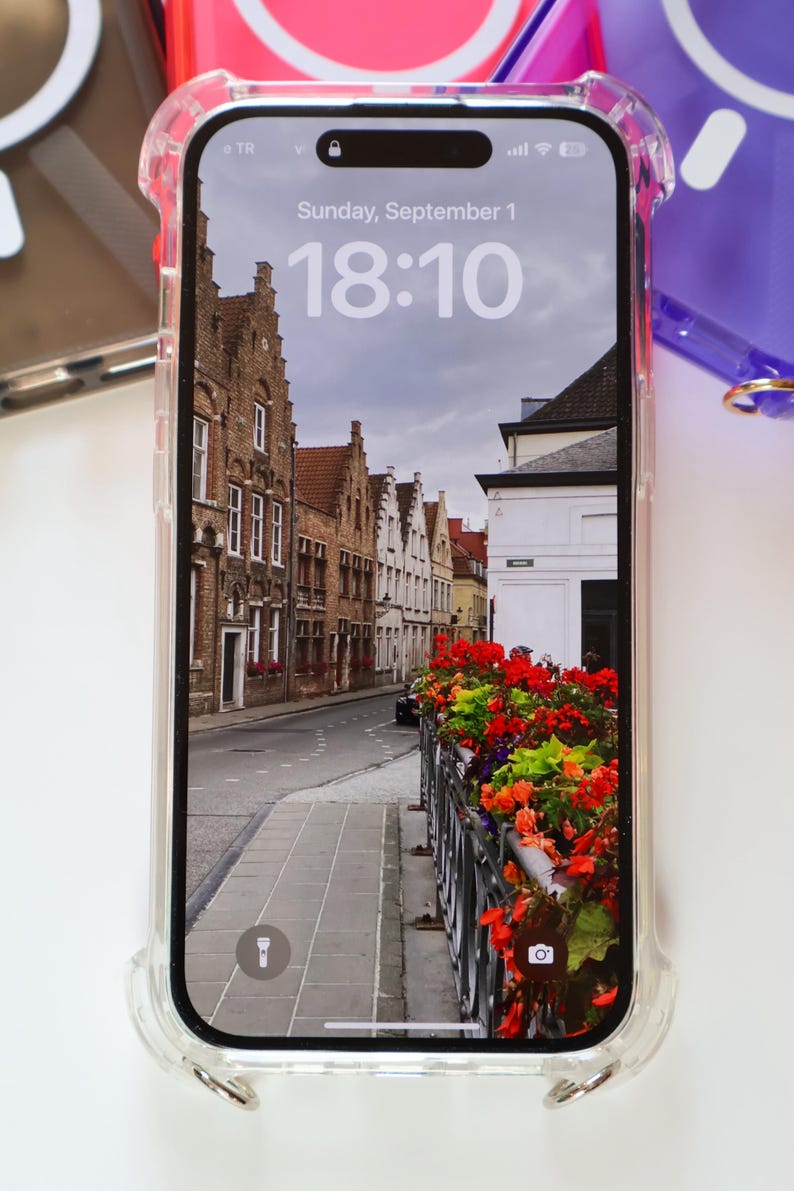 May include: A clear phone case with a raised bumper protects a smartphone displaying a photo of a street in a European city. The time on the phone screen is 18:10. The date is Sunday, September 1.