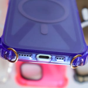 May include: A clear purple phone case with gold rings on the sides. The case has a raised circle on the back.