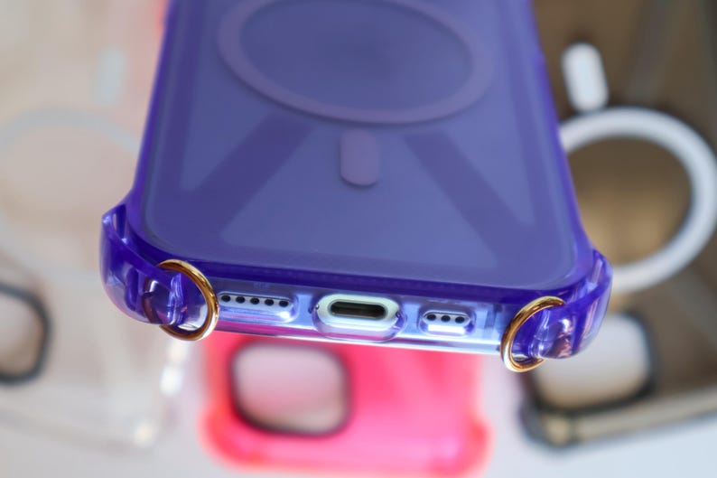 May include: A clear purple phone case with gold rings on the sides. The case has a raised circle on the back.