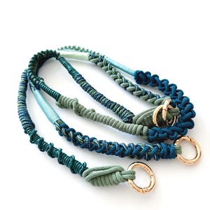 May include: Four macrame dog lead accessories in shades of blue and green, with gold-coloured metal clasps. The leads are made of braided rope and are arranged diagonally against a white background. The colours include teal, navy, and olive green.