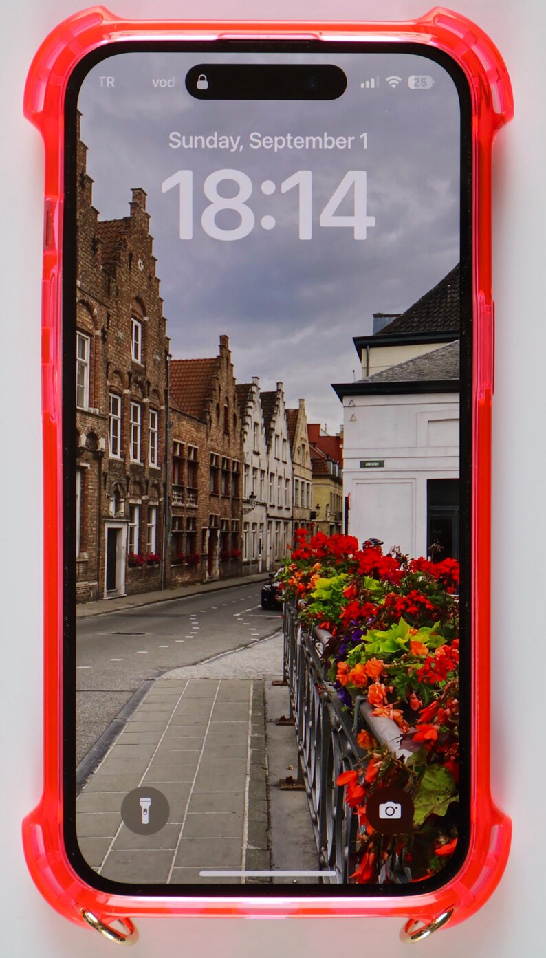 May include: A red phone case with a clear back showing a phone screen with a photo of a street in a European city. The time on the screen is 18:14. The date is Sunday, September 1.