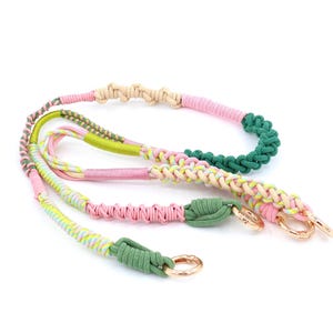 May include: A colorful, braided lanyard in shades of pink, green, yellow, and beige. The lanyard features a variety of textures and patterns, with gold-colored metal clasps. The design is intricate and eye-catching, suitable for keys or accessories.