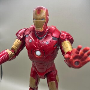 May include: Red and gold Iron Man action figure with a light-up chest and eyes. The figure is posed with one arm outstretched and the other arm bent at the elbow.