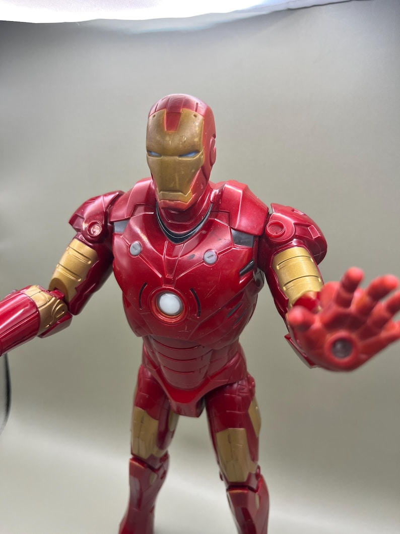 May include: Red and gold Iron Man action figure with a light-up chest and eyes. The figure is posed with one arm outstretched and the other arm bent at the elbow.