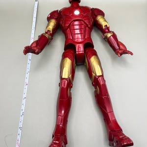 May include: A red and gold Iron Man action figure with articulated limbs. The figure is standing on a white surface.