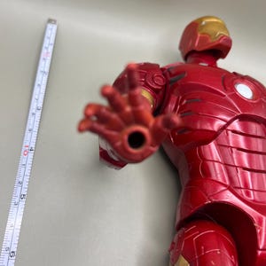 May include: Red and gold Iron Man action figure with articulated arms and legs. The figure is posed with its right hand outstretched.