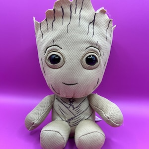 May include: A brown plush toy of the character Groot from the Guardians of the Galaxy movie franchise. The toy has a textured fabric and a friendly expression.