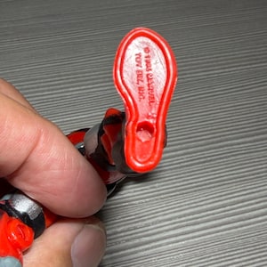 May include: Close-up of a red plastic action figure foot. The foot is stamped with the text "&copy; 1993 MARVEL" and "TOY BIZ, INC." The figure is red, black, and gray.