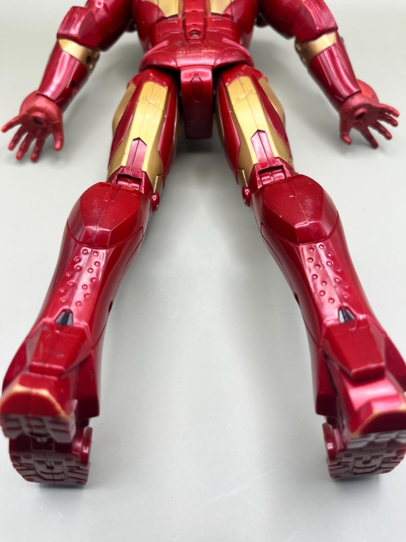 May include: Red and gold action figure of Iron Man with articulated limbs. The figure is posed with its legs spread apart and its arms outstretched. The figure is made of plastic and has a detailed paint job.