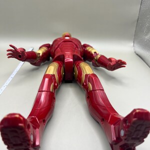 May include: Red and gold Iron Man action figure with articulated limbs. The figure is posed with its legs spread apart and its arms outstretched.