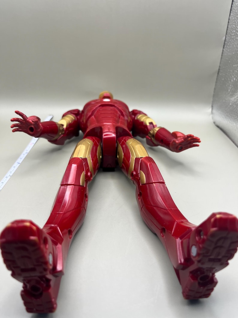 May include: Red and gold Iron Man action figure with articulated limbs. The figure is posed with its legs spread apart and its arms outstretched.