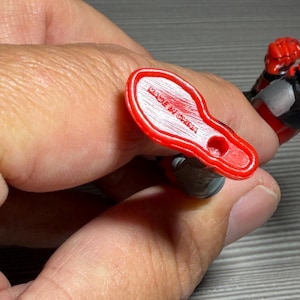 May include: A red plastic foot of an action figure, with the words "MADE IN CHINA" printed on the sole. The figure's leg is gray and black. The figure is held by a person.