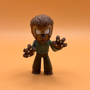 May include: A stylized figurine of a werewolf with a brown fur-like head and hands, wearing a green shirt and brown pants. The figure has a stern expression and is posed with its hands outstretched. The figurine is on an orange background.