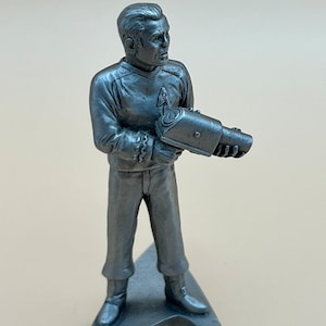 May include: A pewter figurine of a Star Trek character holding a phaser. The figurine is standing on a triangular base with the Star Trek logo.