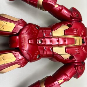 May include: Red and gold Iron Man action figure with articulated limbs. The figure has a detailed chest plate with a silver design and the words "ASSEMBLED IN CHINA MADE IN CHINA" printed on the side.
