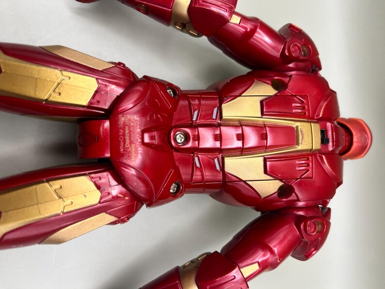 May include: Red and gold Iron Man action figure with articulated limbs. The figure has a detailed chest plate with a silver design and the words "ASSEMBLED IN CHINA MADE IN CHINA" printed on the side.