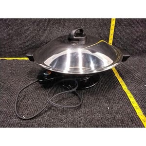 Könnte beinhalten: Ein elektrischer Wok aus Edelstahl mit schwarzem Boden und Deckel. Der Wok hat einen schwarzen Griff am Deckel und zwei Seitengriffe. Ein schwarzes Netzkabel und ein Temperaturregler sind sichtbar.